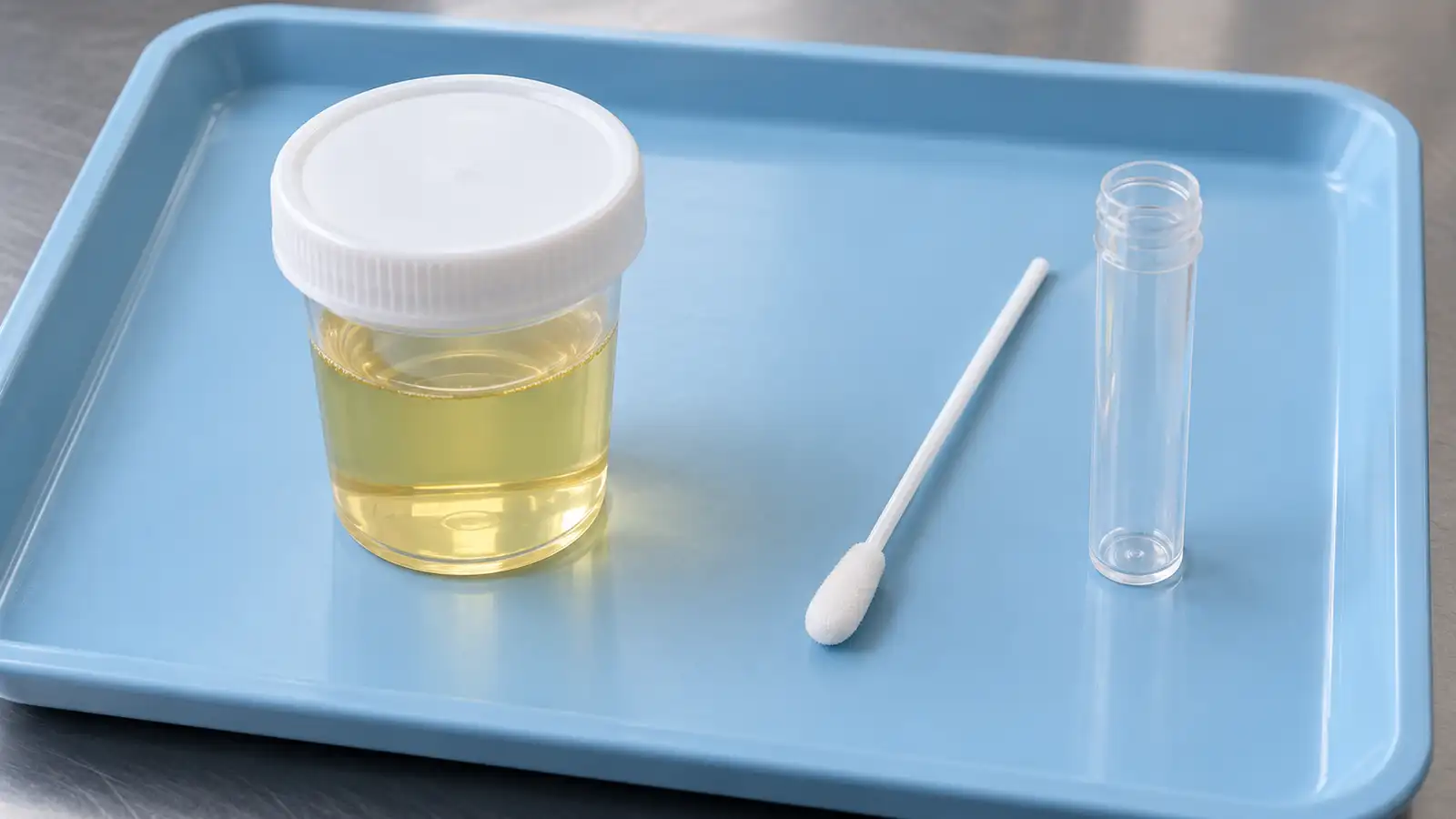 A sealed urine sample cup sits beside an oral swab and clear collection tube.