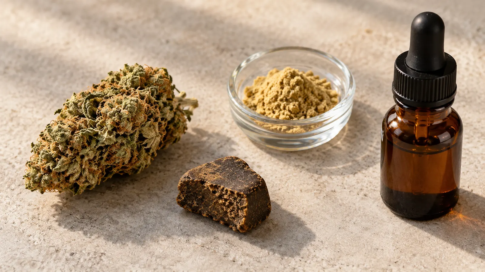 Cannabisblomst, hash, kief og en umærket ravfarvet dråbeflaske ligger på en stenoverflade.