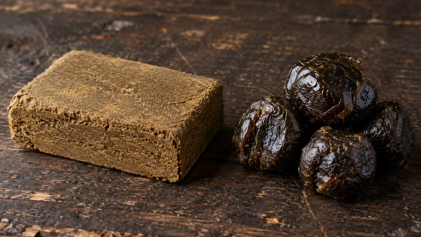 Pressed hashish block next to dark hand-rubbed charas balls, showing the difference in texture and color
