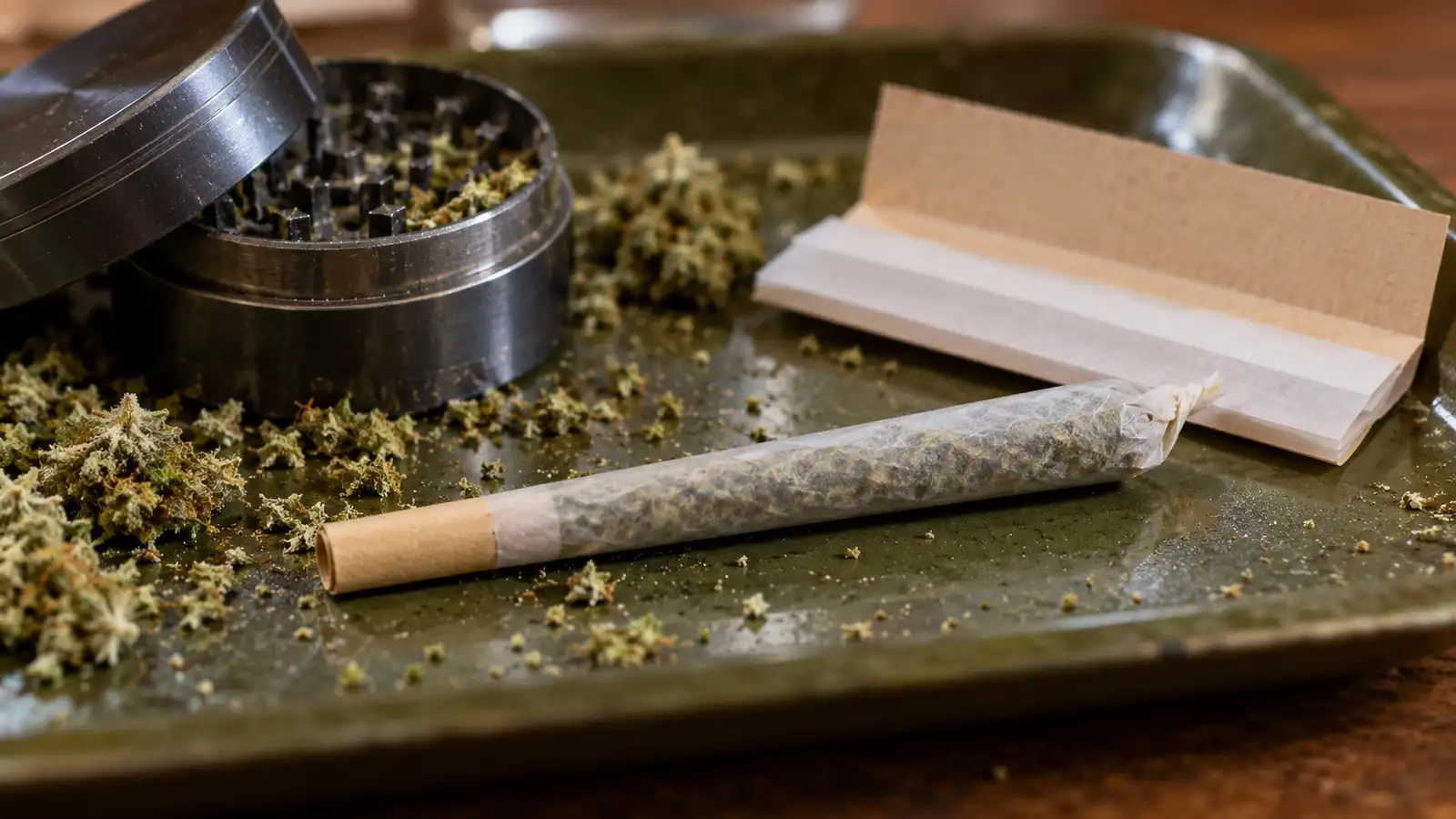 Hand-rolled joint with a cardboard filter tip on a rolling tray next to papers and a grinder